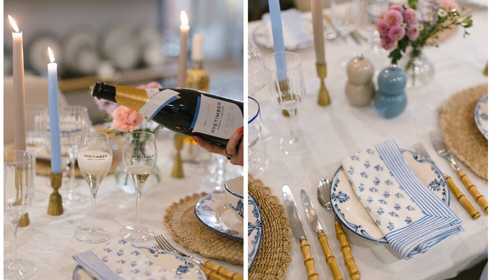 A beautiful pastel blue and pink tablescape design with pattern table linen, brass homeware accessories, flowers and a bottle of Nyetimber